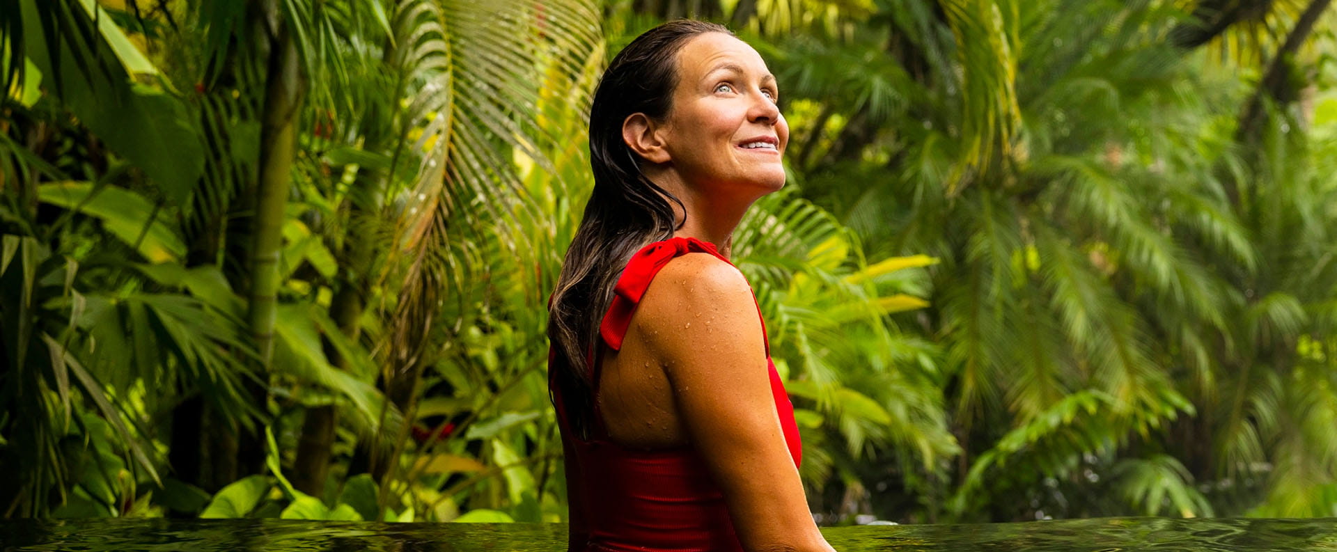 Woman standing in waist-height water in a rainforest environment and smiling while looking in wonder at the trees.
