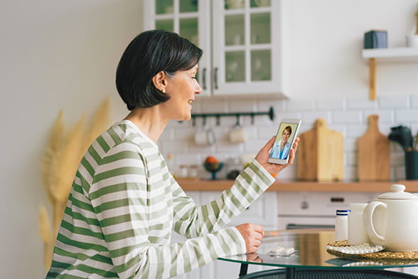 Woman sitting at kitchen table talking to a doctor via video call