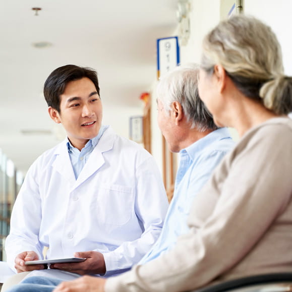 Doctor sat down with two elderly patients in hospital hallway