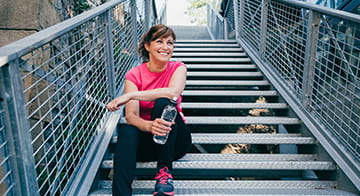 Woman in exercise clothes, sitting on steps with a bottle of water, taking a rest after a workout