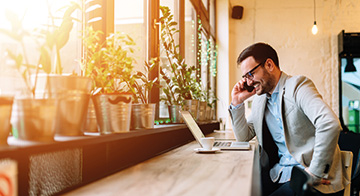 Man drinking coffee on phone with laptop