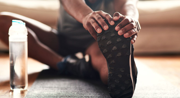 Close up image of person sitting on the floor and stretching leg after exercise