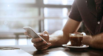 Man sits at table using mobile phone with coffee